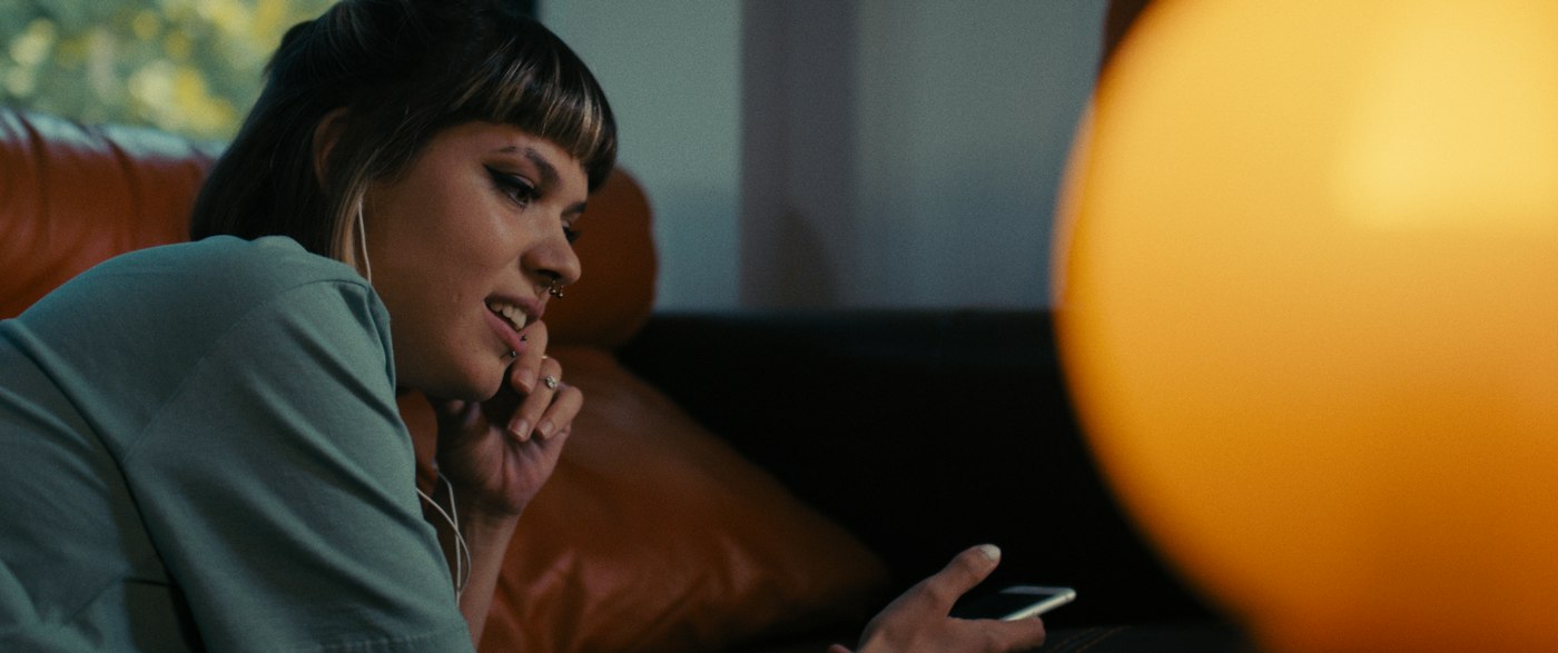 A woman on a couch at night, smiling, phone in hand
